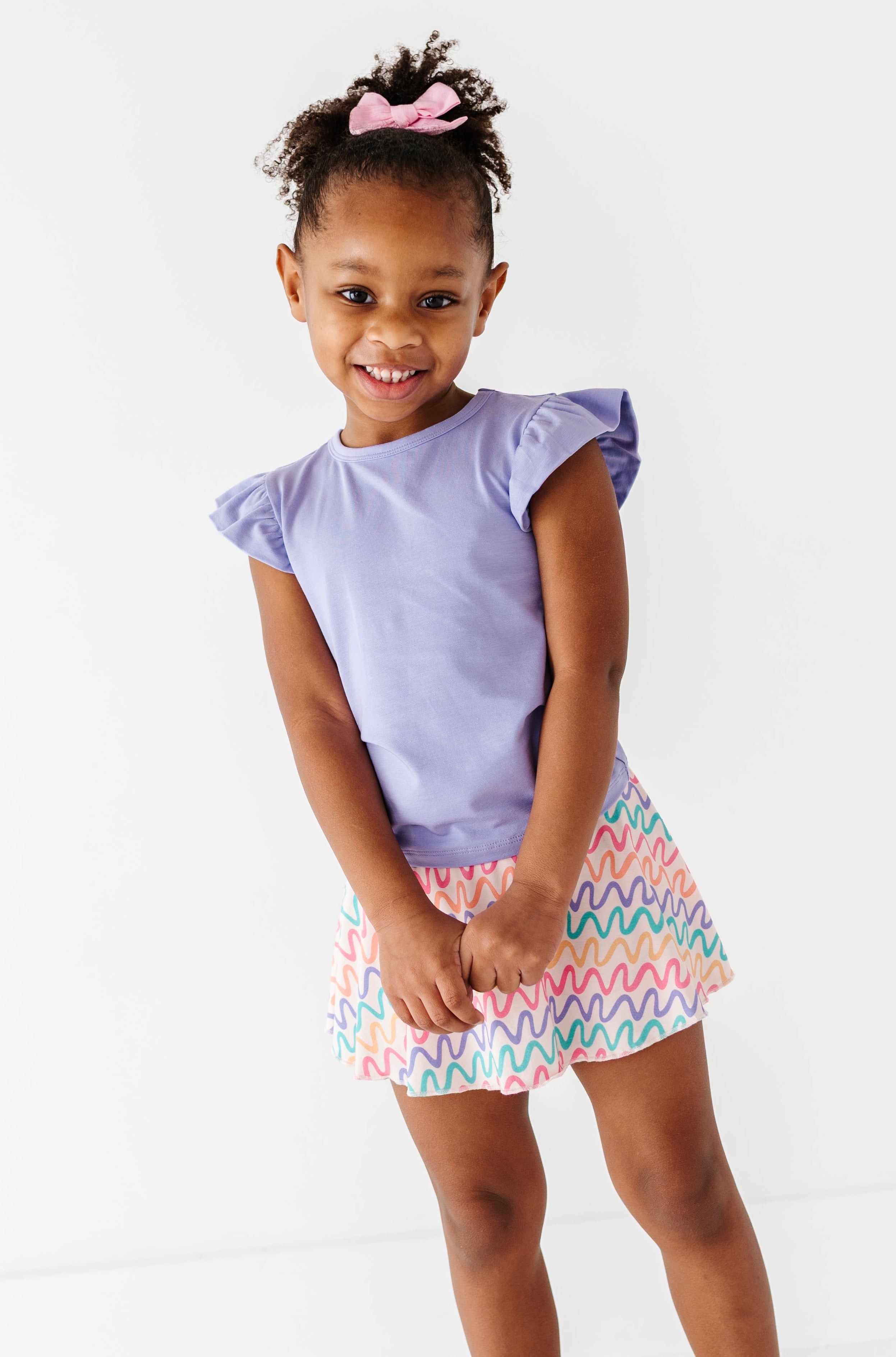 Young girl wearing a bamboo/cotton lilac top and colorful bamboo skort on a white background